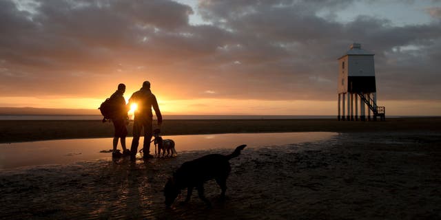 People photograph the S near to the lighthouse at Burnham-on-Sea, Somerset, as the sun sets an hour earlier after the clocks went back one hour last night due to the end of Daylight Saving Time.