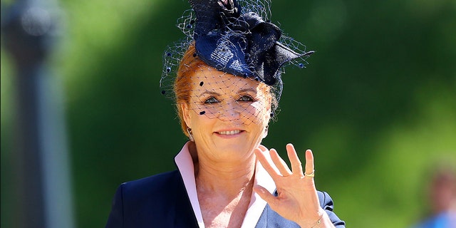 Sarah Ferguson waves in a navy suit, light pink top, and navy hat as she arrives for the royal wedding of Meghan Markle and Prince Harry