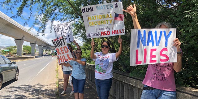 Protestors upset with the Department of Defense's response to the leak of jet fuel into the water supply hold signs outside the gate at Joint Base Pearl Harbor-Hickam, Hawaii, on Sept. 30, 2022.