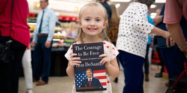 A child holds Republican Florida Gov. Ron DeSantis' new book during a surprise signing at a Daytona Beach Buc-ee's March 2, 2023.