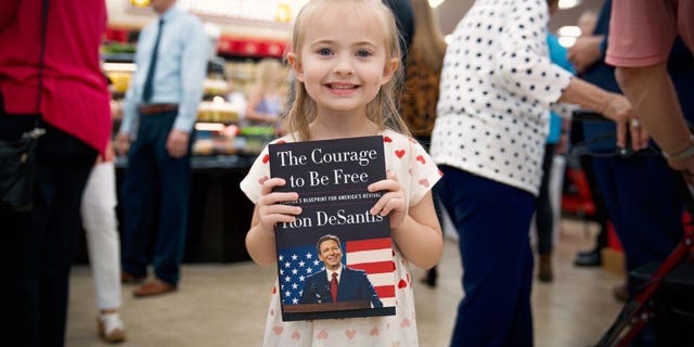 A child holds Republican Florida Gov. Ron DeSantis' new book during a surprise signing at a Daytona Beach Buc-ee's March 2, 2023.