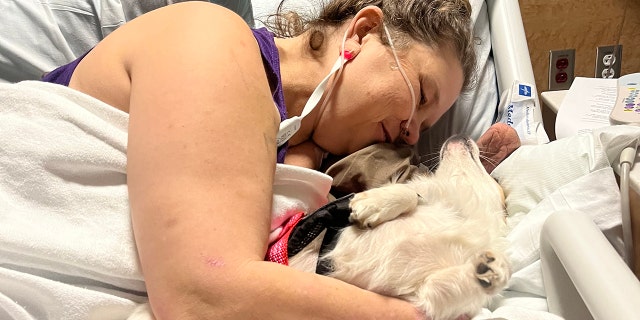 Texas mom suffers quadruple amputation, credits her faith and a little dog for pulling her through 6 Adkins cuddles her dog Mazi in a hospital bed after a recent procedure.