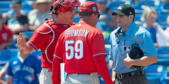 El receptor abierto de los Philadelphia Phillies, JT Realmuto, y el manager Rob Thomson discuten con el árbitro Randy Rosenberg después de que Realmuto fuera expulsado de un juego de béisbol de entrenamiento de primavera en Dunedin, Florida, el lunes 27 de marzo de 2023.