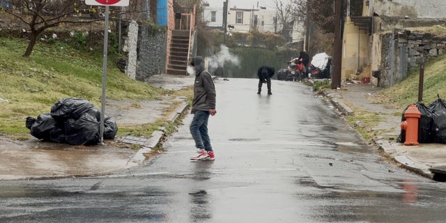An addict stands in the middle of the street slumped over, struggling to remain upright.