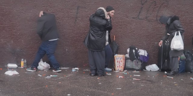 Addicts line a wall in Kensington. One sways and seems to struggle to remain standing.