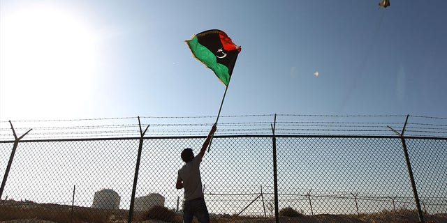 FILE: A man waves a Libyan flag as fighter jet flies by at the Zueitina oil terminal