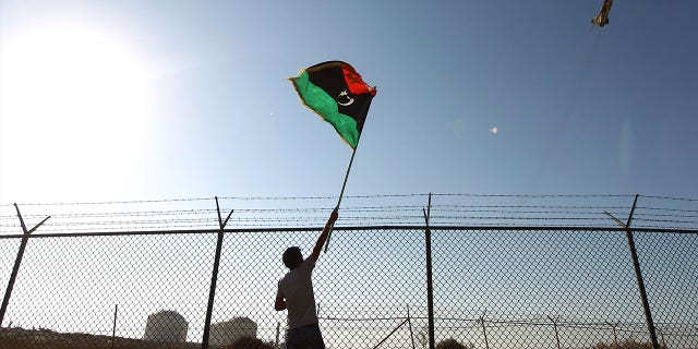 FILE: A man waves a Libyan flag as fighter jet flies by at the Zueitina oil terminal