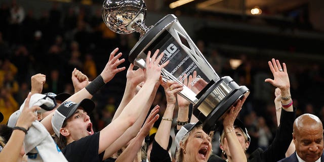 L'entraîneur-chef de l'Iowa, Lisa Bluder, au centre, soulève le trophée avec l'aide de la garde Caitlin Clark, à gauche, après avoir battu l'État de l'Ohio lors du match de championnat de basket-ball universitaire de la NCAA du tournoi féminin Big Ten, dimanche 5 mars 2023, à Minneapolis.