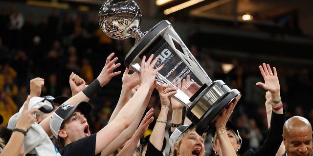 La entrenadora en jefe de Iowa, Lisa Bluder, en el centro, levanta el trofeo con la ayuda de la escolta Caitlin Clark, a la izquierda, después de derrotar a Ohio State en un juego de campeonato de baloncesto universitario de la NCAA durante el Torneo Big Ten Femenino el domingo 5 de marzo de 2023 en Minneapolis.