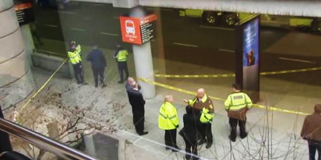 Investigators stand near the scene at Logan Airport where a Massachusetts man was struck and killed by a coach bus. A bus sign can be seen on one of the pillars where crime scene tape is wrapped around.
