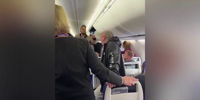 The man in the sports jacket is seen confronting the heavily tattooed man and other passengers. A Southwest Airlines flight attendant is seen standing between the two men.