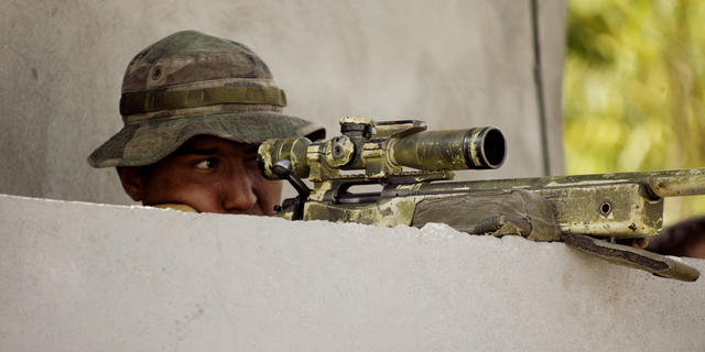 A United States Marine scout sniper looks through the scope of his rifle as he is perched above a gate of the industrial park March 12, 2004, in Port-au-Prince, Haiti. The Marines recently announced the role will be removed from its infantry battalions.