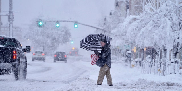 A passer-by uses an umbrella while crossing a snow-covered street, Tuesday, March 14, 2023, in Pittsfield, Mass. 