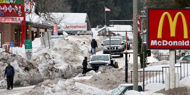 La gente camina por una calle arada después de que una serie de tormentas invernales arrojaran más de 100 pulgadas de nieve en las montañas de San Bernardino en el sur de California el 6 de marzo de 2023, en Crestline, California. 
