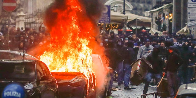 Supporters of the Eitracht Frankfurt soccer team set a police car afire as they clash with police Wednesday, March 15, 2023 in Naples, Italy, where their team is about to play a Champions League, round of 16, second leg soccer match against Naples.