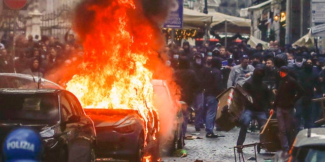 Aficionados del equipo de fútbol Eitracht Frankfurt prendieron fuego a un coche de policía mientras chocaban con la policía el miércoles 15 de marzo de 2023 en Nápoles, Italia, donde su equipo está a punto de jugar un partido de fútbol de vuelta de los octavos de final de la Liga de Campeones contra Nápoles .