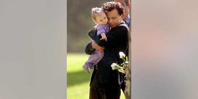Robert Blake hugs his 11-month-old daughter, Rose Lenore Blake, as she reaches for a white rose picked from the coffin bearing her mother, Bonny Lee Bakley, during a funeral ceremony on May 25, 2001.