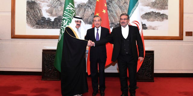 Ali Shamkhani, secretary of Iran's Supreme National Security Council, right, shakes hands with Saudi national security adviser Musaad bin Mohammed al-Aiban, left, as Wang Yi, China's most senior diplomat, looks on in Beijing on March 11, 2023.