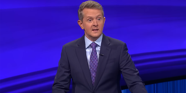 Ken Jennings in a navy suit with a light blue shirt and purple suit on the set of 'Jeopardy!'