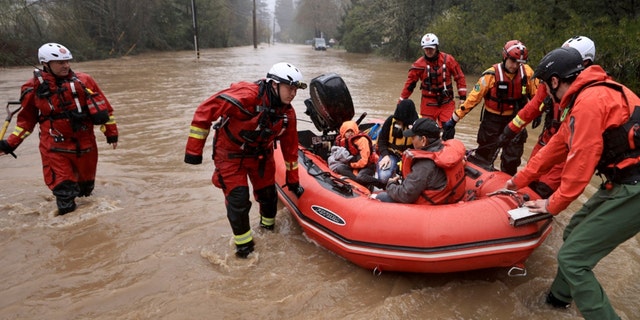 Sonoma County Fire District firefighters and a sheriff's deputy pull people in the back of the boat and the driver of a van whose vehicle stalled out in high water on Armstrong Woods Road in Guerneville, Calif., Tuesday, March 14, 2023. 