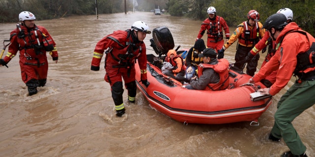 Sonoma County Fire District firefighters and a sheriff's deputy pull people in the back of the boat and the driver of a van whose vehicle stalled out in high water on Armstrong Woods Road in Guerneville, Calif., Tuesday, March 14, 2023. 