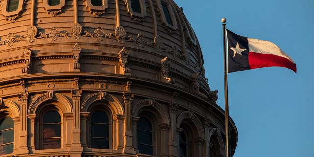 Texas Capitol building dome with the Texas flag waving in front.