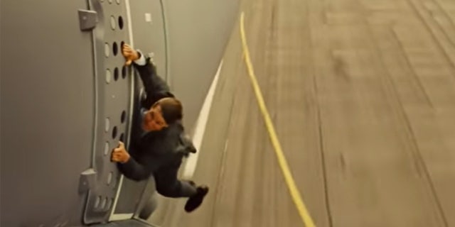 Tom Cruise hanging off the side of a plane in a stunt for Mission Impossible Rogue Nation