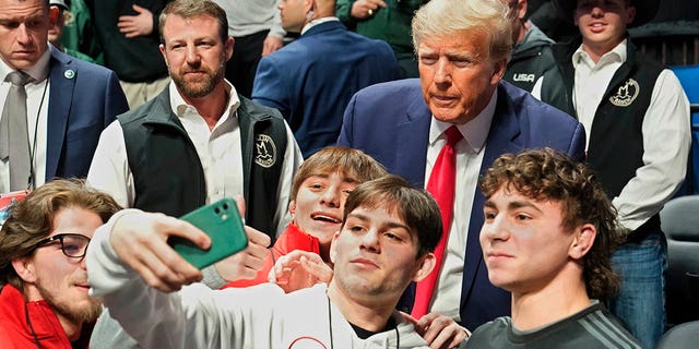 Former President Donald Trump, right, poses for photos at the NCAA Championship Wrestling Championship, Saturday, March 18, 2023, in Tulsa, Oklahoma.