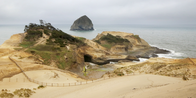 FILE- View of the safety fence along the summit of Cape Kiwanda, with views of the ocean and Haystack Rock in the distance.