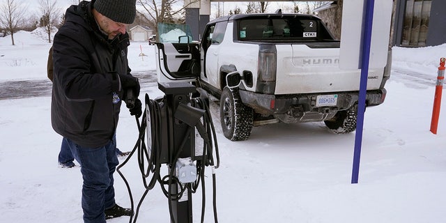 Lawrence Ziehr, project manager for energy recovery on GM's electric vehicles, connects a Hummer EV to a charging station, Wednesday, Feb. 22, 2023, in Sault Ste. Marie, Mich. Some automakers and drivers fear lower battery range in the cold could limit acceptance of electric cars, trucks and buses, at a time when emissions from transportation must go down sharply to address climate change.  (AP Photo/Carlos Osorio)