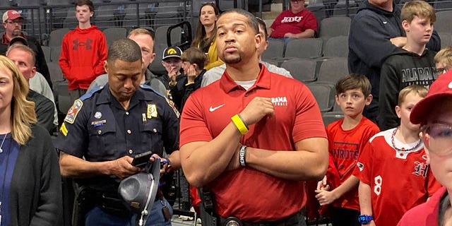 An unidentified armed security guard, wearing a crimson Alabama basketball shirt, watches as Alabama practices at the NCA college basketball tournament, Wednesday, March 15, 2023, in Birmingham, Ala.