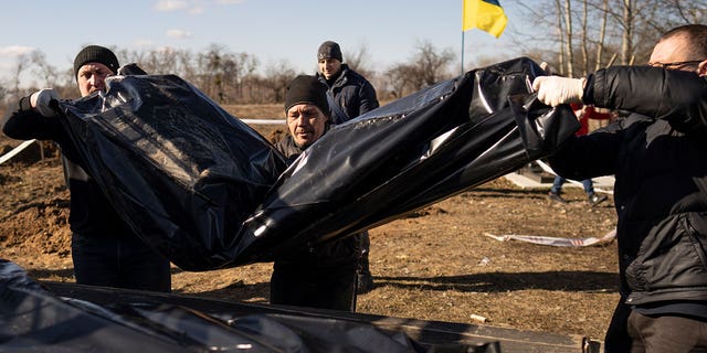 Men carry bags containing three freshly exhumed bodies in a Ukrainian cemetery on March 2, 2023. Ukrainian authorities are still exhuming the bodies of civilians hastily buried in makeshift graves. 