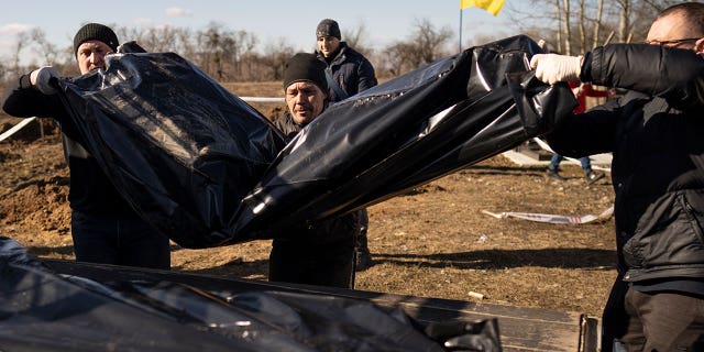 Men carry bags containing three freshly exhumed bodies in a Ukrainian cemetery on March 2, 2023. Ukrainian authorities are still exhuming the bodies of civilians hastily buried in makeshift graves.