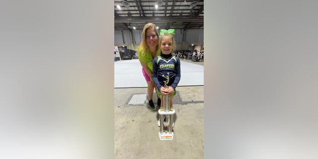 Holding onto her first place trophy, eight-year-old Peyton Thorsby, gets congratulations from her cheer coach Nikki Melucci. 