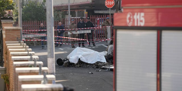 The burned remains of one of the two Italian Air Force aircrafts that crashed in Guidonia on March 7, 2023, is covered with a white cloth.