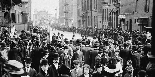 Crowds of people stand in the street, waiting to identify bodies of immigrant workers who perished in the Triangle fire in New York City on March 25, 1911. 