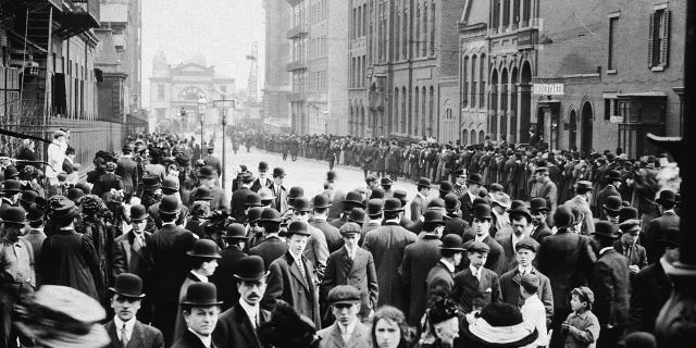 Crowds of people stand in the street, waiting to identify bodies of immigrant workers who perished in the Triangle fire in New York City on March 25, 1911.