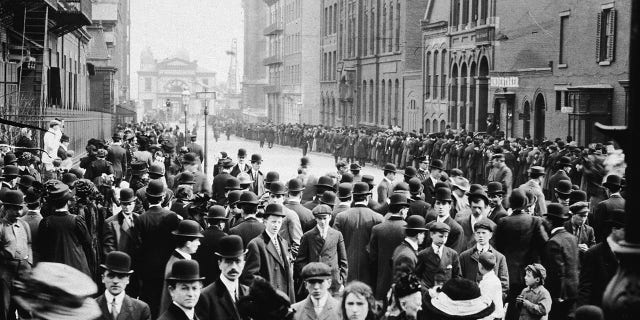 Crowds of people stand in the street, waiting to identify bodies of immigrant workers who perished in the Triangle fire in New York City on March 25, 1911. 