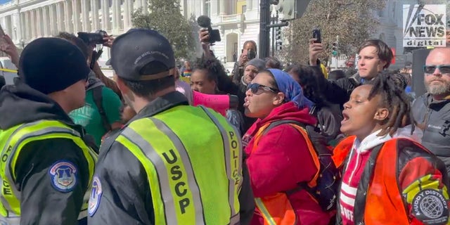 Protesters shout at police officers for causing violence after a woman was handcuffed for allegedly defacing the sidewalk. 