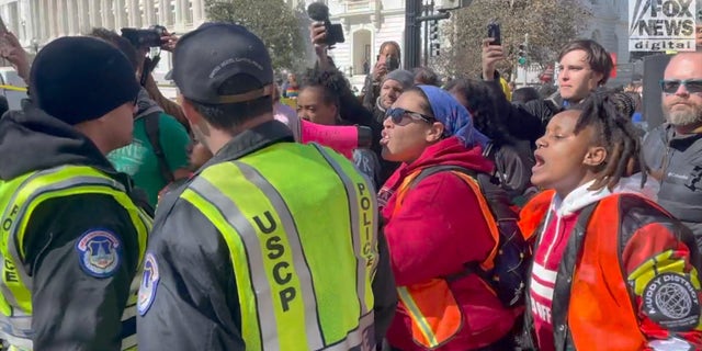 Protesters shout at police officers for causing violence after a woman was handcuffed for allegedly defacing the sidewalk.