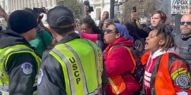 Protesters shout at police officers for causing violence after a woman was handcuffed for allegedly defacing the sidewalk. 