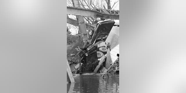 A mangled car is freed from its watery grave as a worker directs the operation from part of the wrecked Silver Bridge.