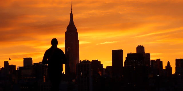 The sun rises behind the Empire State Building in New York City as a person walks on a pier in the Hudson River on March 10, 2023, in Hoboken, New Jersey. 