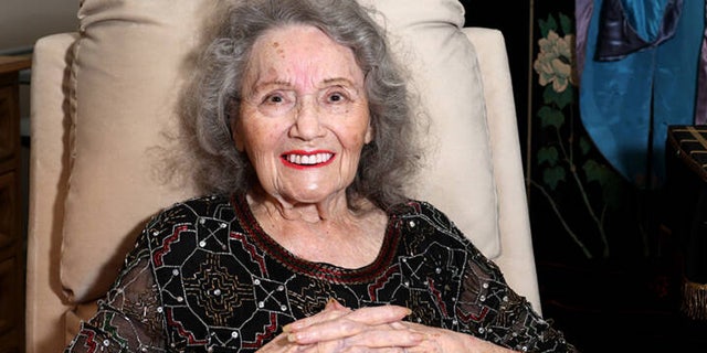 Gloria Dea sits in a chair at her home