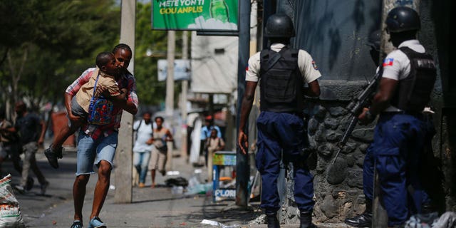 A parent, carrying his child after picking him up from school, runs past police carrying out an operation against gangs in the Bel-Air area of Port-au-Prince, Haiti, on March 3, 2023.