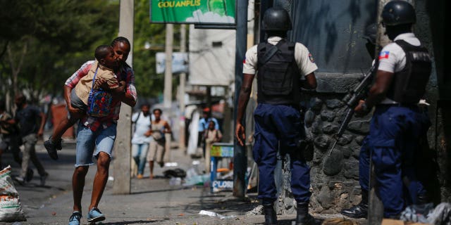 A parent, carrying his child after picking him up from school, runs past police carrying out an operation against gangs in the Bel-Air area of Port-au-Prince, Haiti, on March 3, 2023.