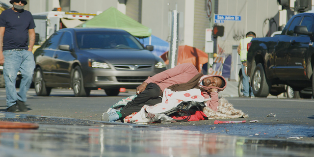 A man sleeps atop a pile of belongings in the street as The City of Los Angeles moves a homeless encampment.