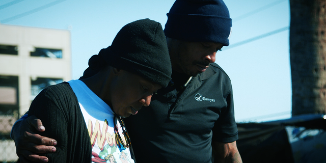 Aisha and James look down at their destroyed belongings following a fire at a homeless encampment in Phoenix, Arizona.  