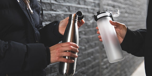 Two women are shown holding reusable water bottles — on the left, a screw-top version, and on the right, a spout-top bottle.