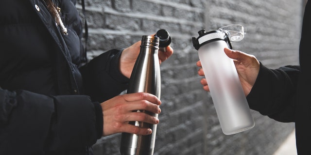 Two women are shown holding reusable water bottles — on the left, a screw-top version, and on the right, a spout-top bottle.
